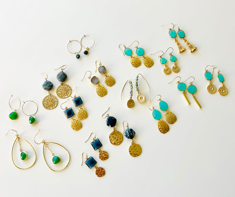 Multiple pairs of gold drop earrings featuring various gemstones on a white background.